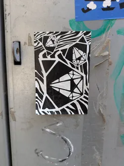 A black and white sticker with geometric shapes that resemble gems, placed against a background of zebra-like stripes. The design is modern and eye-catching, making it stand out against the metallic surface it is affixed to.