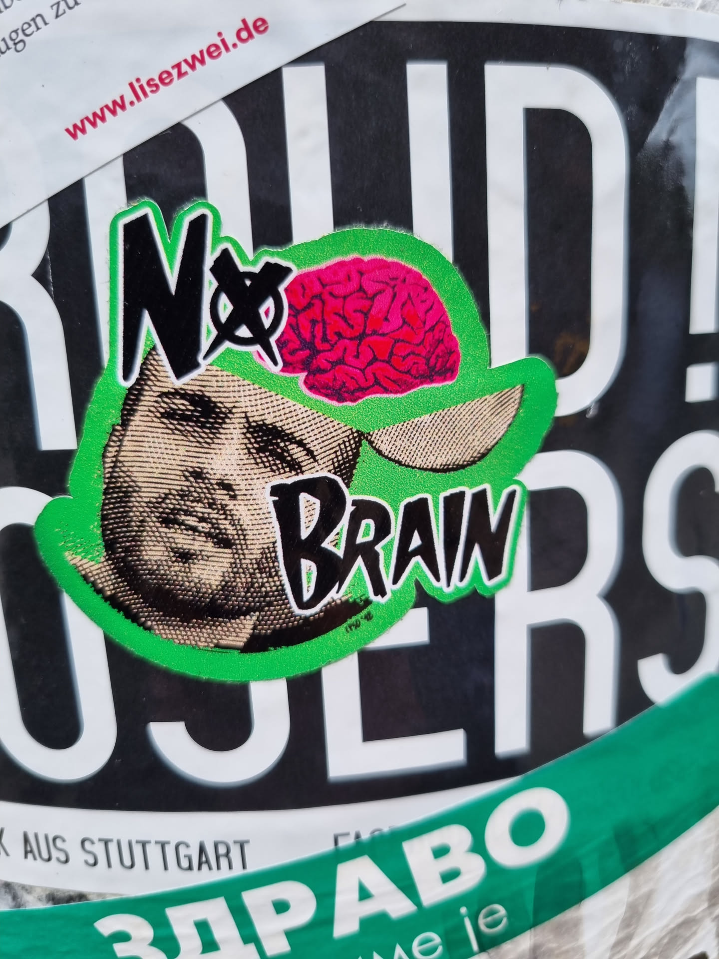 A sticker with a graphic of a man's face wearing a cap with a brain on it. The text 'No Brain' is written on the sticker.  The style is reminiscent of punk or protest art.