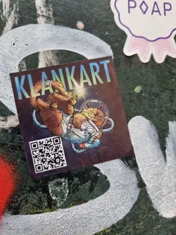 A sticker featuring an illustration of a cat dressed as an astronaut floating in space. The artist's name, Klankart, is prominently displayed at the top, along with a QR code near the bottom.