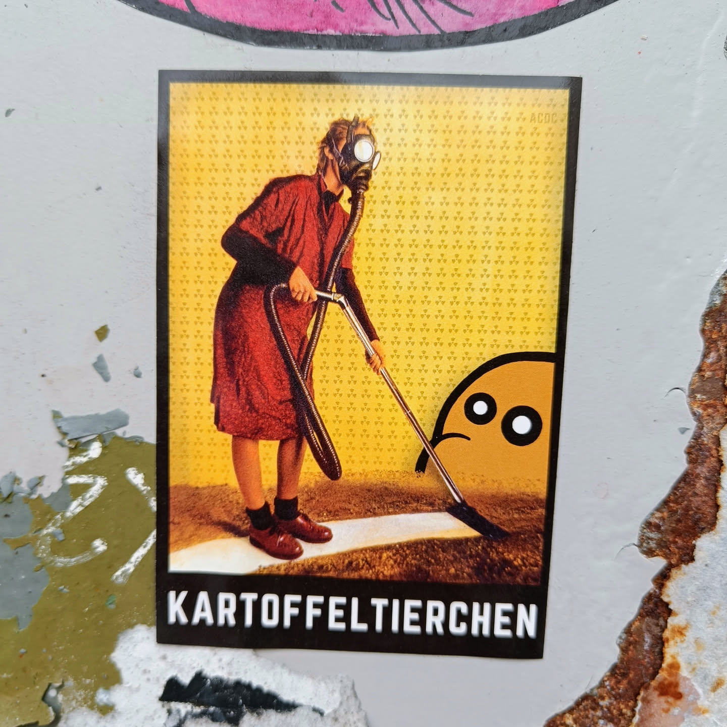 A sticker depicting a person wearing a gas mask and using a vacuum cleaner to clean up after a small, sad-looking character. The text at the bottom of the sticker says "Kartoffeltierchen."