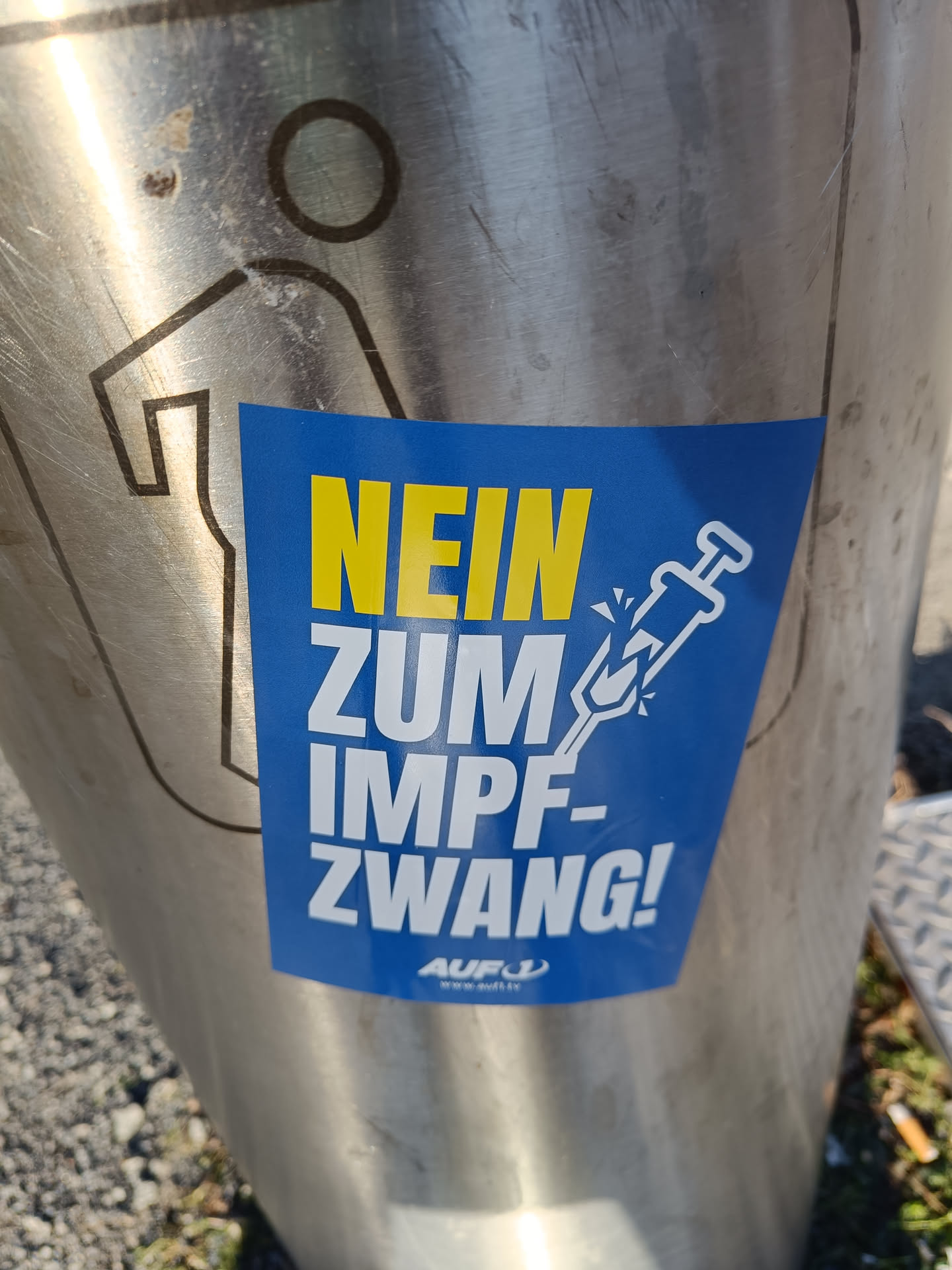 A blue sticker with the text "Nein zum Impfzwang!" (No to mandatory vaccination) and an image of a broken syringe.  The sticker also includes a small logo with the text "AUF1" and a website address.