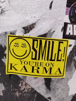 Yellow sticker with a smiley face and the text "SMILE! YOU'RE ON KARMA". The smiley face has Om symbols in its eyes. 