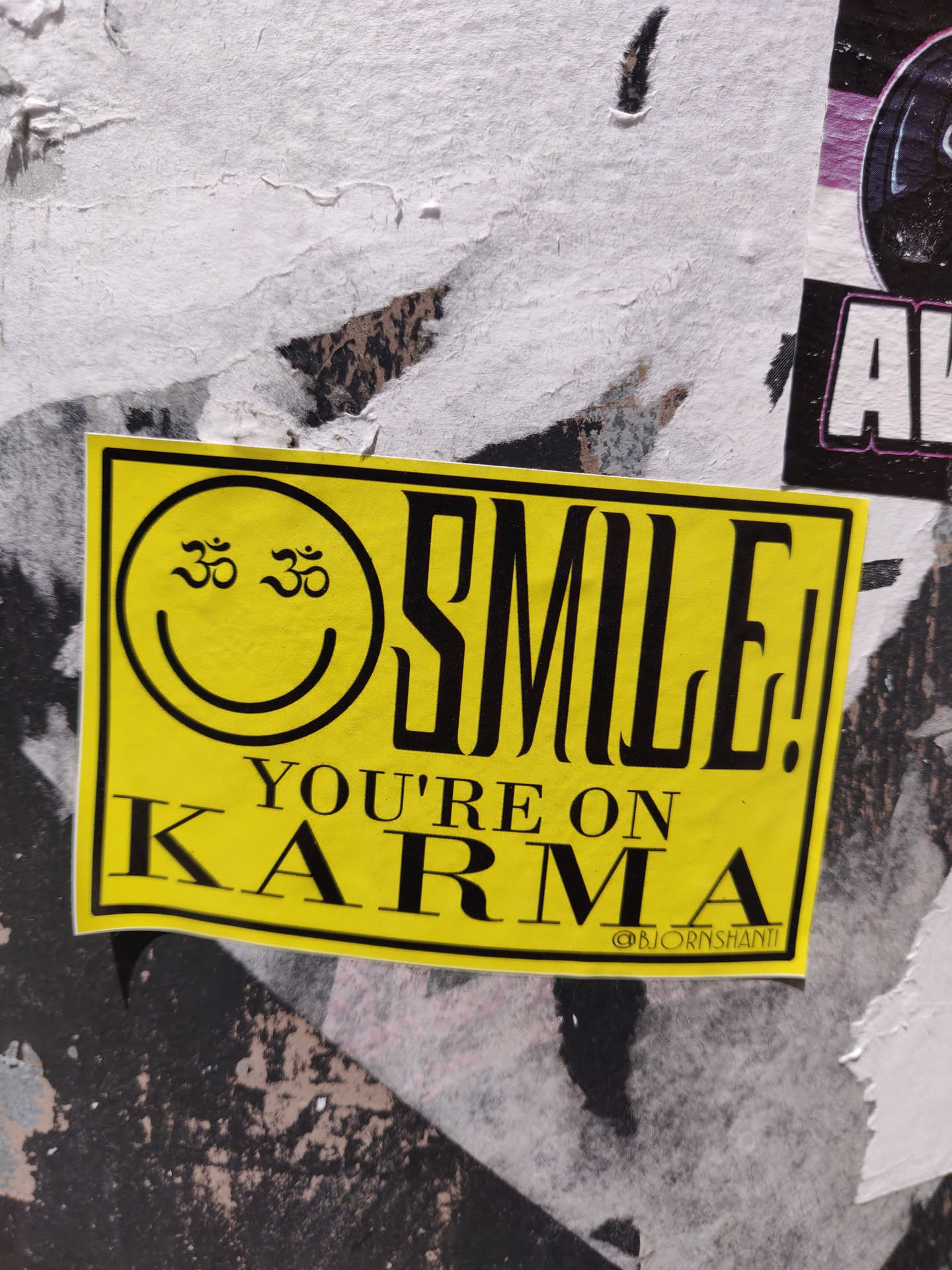 Yellow sticker with a smiley face and the text "SMILE! YOU'RE ON KARMA". The smiley face has Om symbols in its eyes. 