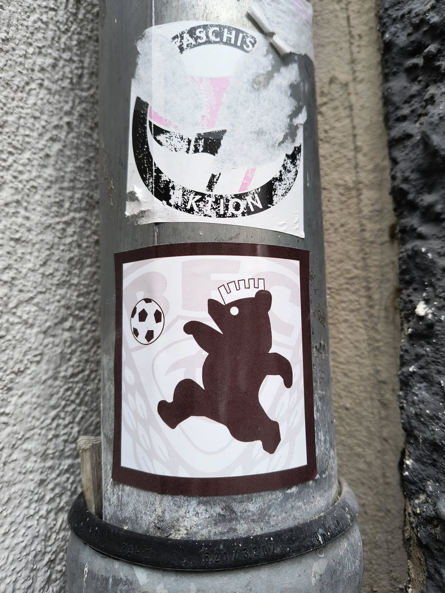 A sticker featuring a playful illustration of a bear kicking a soccer ball. The bear is depicted in a dynamic pose, suggesting movement and action. The sticker has a simple, minimalist design with a color scheme that includes shades of brown and white.