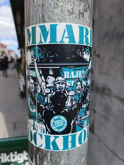 A sticker depicting a lively scene of Hammarby Stockholm supporters celebrating. The illustration showcases a group of enthusiastic fans, arms raised in jubilation, against a backdrop suggesting a stadium atmosphere. The colors are predominantly teal and black, with the words "HAMMARBY" and "STOCKHOLM" prominently displayed, creating a visually striking and dynamic image.