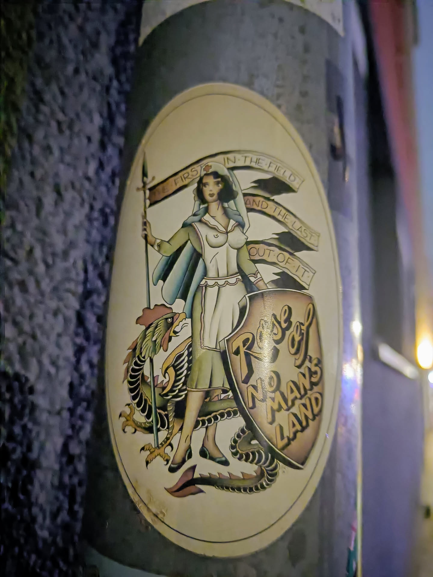 Sticker featuring a vintage illustration of a female nurse standing with a dragon, holding a banner that says 'First in the field and the last out of it'. The background is beige and the style is reminiscent of old-school tattoo art. The words 'Rose of No Man's Land' are prominently displayed on a shield.