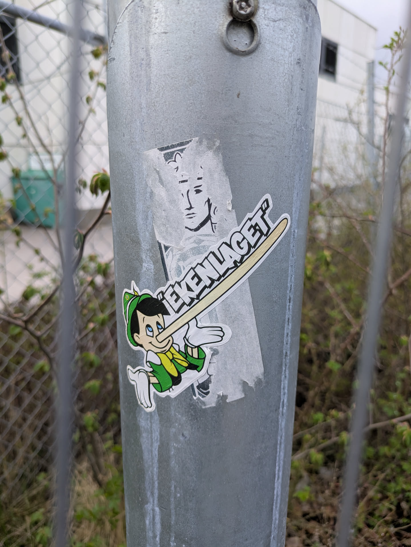 A colorful sticker features a cartoon character that resembles Pinocchio, with a long nose that extends over the head. The text says "EKENLAGET". There's an older, damaged sticker above it showing a monochrome character with long hair.