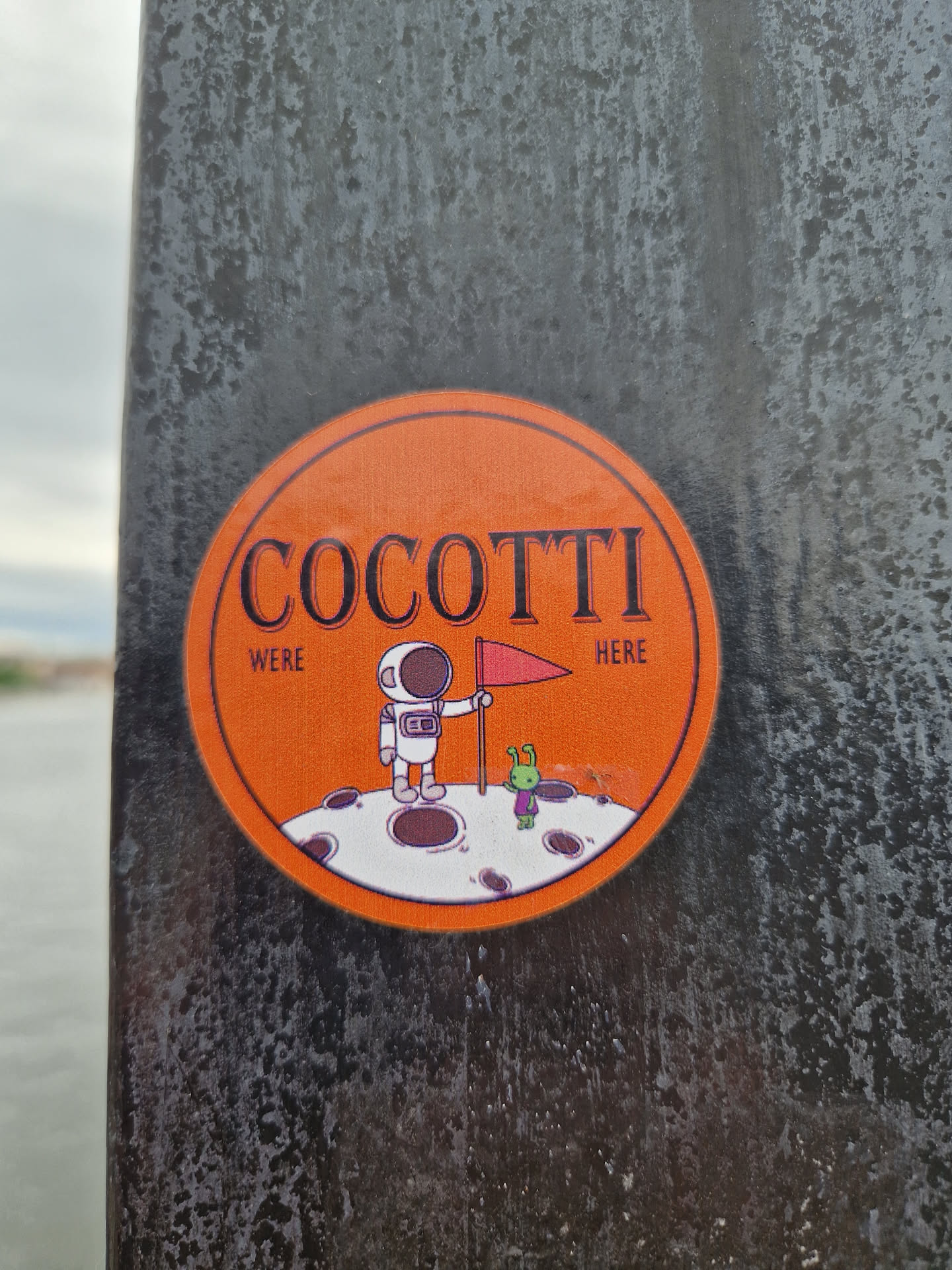 Orange round sticker with illustration of astronaut and alien on the moon.  Text says COCOTTII WERE HERE.
