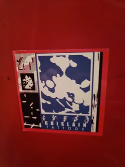 A square sticker with a blue and white abstract design. The text "GHISLAIN TATTOOS" is visible at the bottom. There are also some Chinese characters on the sticker.