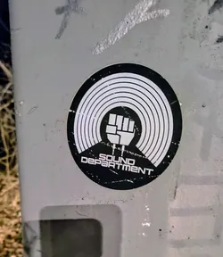 Black and white round sticker with a vinyl record design and a fist in the center. The text "SOUND DEPARTMENT" is written below the fist.