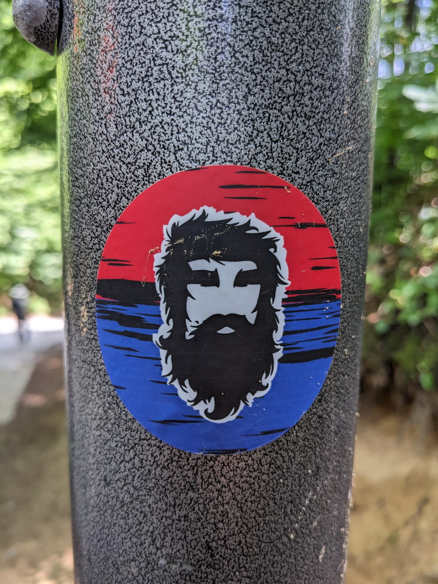 Round sticker featuring a stylized illustration of a man with a beard. The sticker has a red, white, and blue color scheme. 
