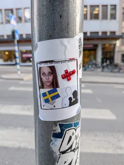 A rectangular white sticker adhered to a grey metal pole, showing slight curling at its edges. The sticker features a central image area with a thin black border. At the top, the text "The 'I only date black guys' starter kit." is printed. Below this, the content is divided into four distinct visual elements against a white background: in the top-left, a close-up photograph of a young woman with dark circles under her eyes; in the top-right, red letter blocks spelling out "AIDS" horizontally and "HIV" vertically, intersecting at the 'I'; in the bottom-left, a small image of the Swedish flag placed inside a wire shopping cart; and in the bottom-right, a black silhouette of a family (man, woman, and child). A partial QR code is visible on the top-right edge of the sticker, outside the main content frame.