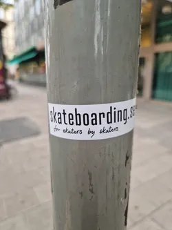 A white sticker on a grey pole. The text on the sticker says 'skateboarding.se for skaters by skaters'.