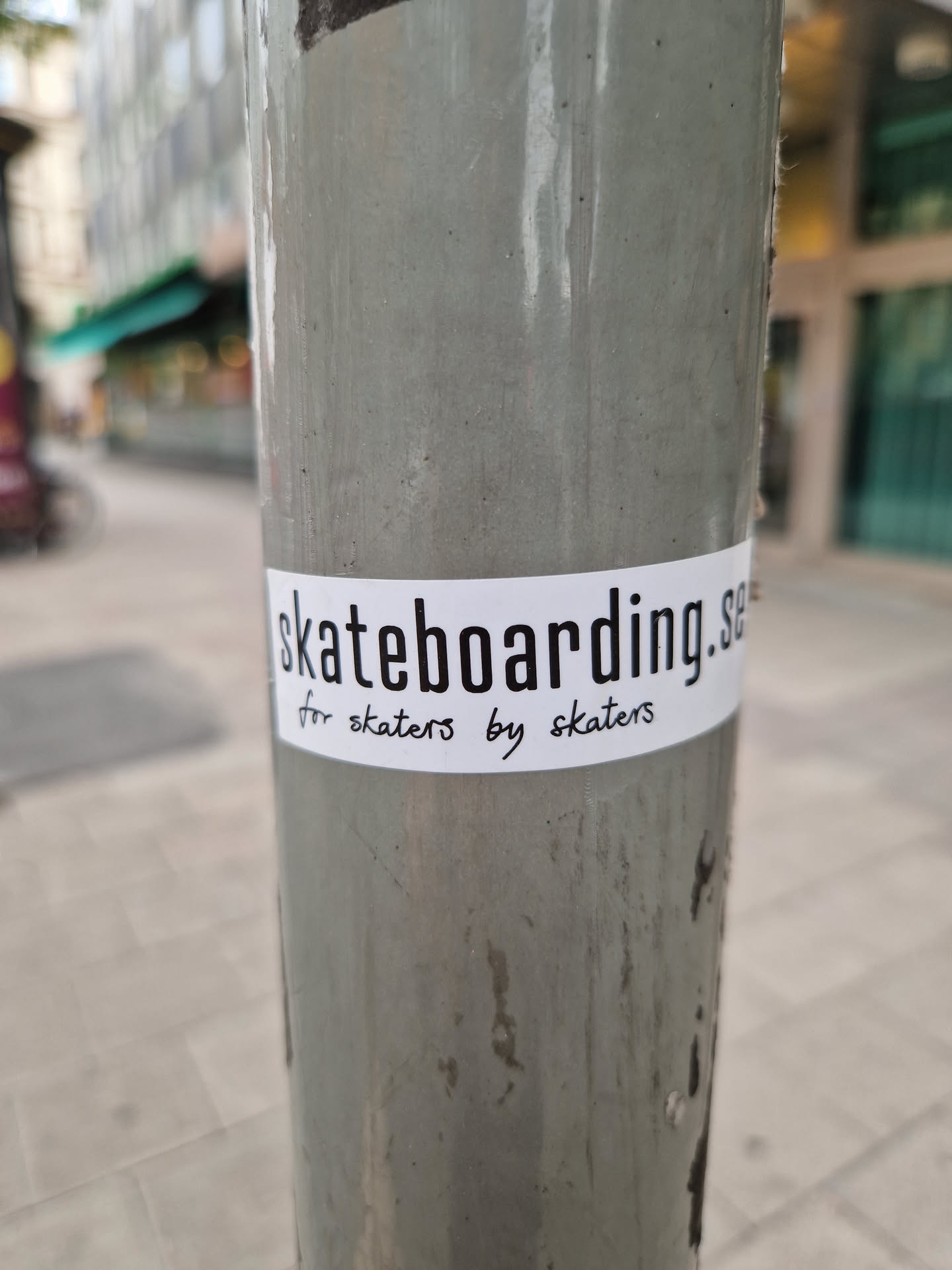 A white sticker on a grey pole. The text on the sticker says 'skateboarding.se for skaters by skaters'.