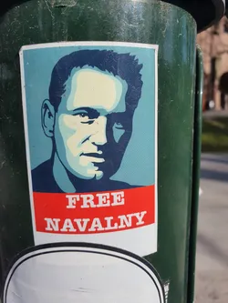 A sticker featuring a stylized portrait of Alexei Navalny with the text "FREE NAVALNY" in red letters on a blue background.  The style is reminiscent of protest art.