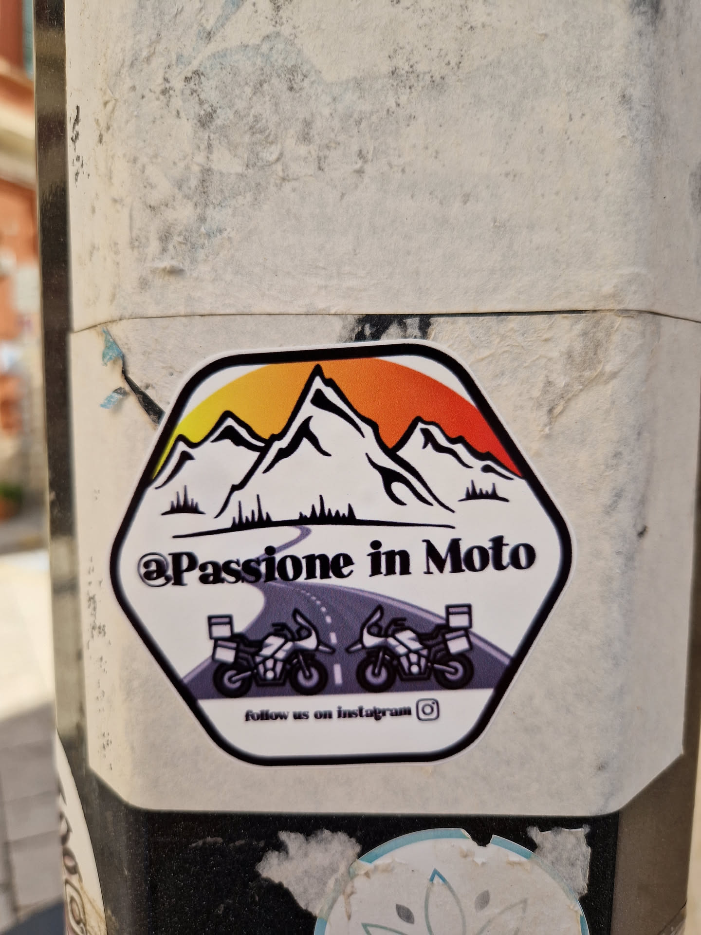 Hexagon sticker featuring a sunset mountain landscape with two motorcycles on a road. Text includes '@Passione in Moto' and 'follow us on Instagram'.