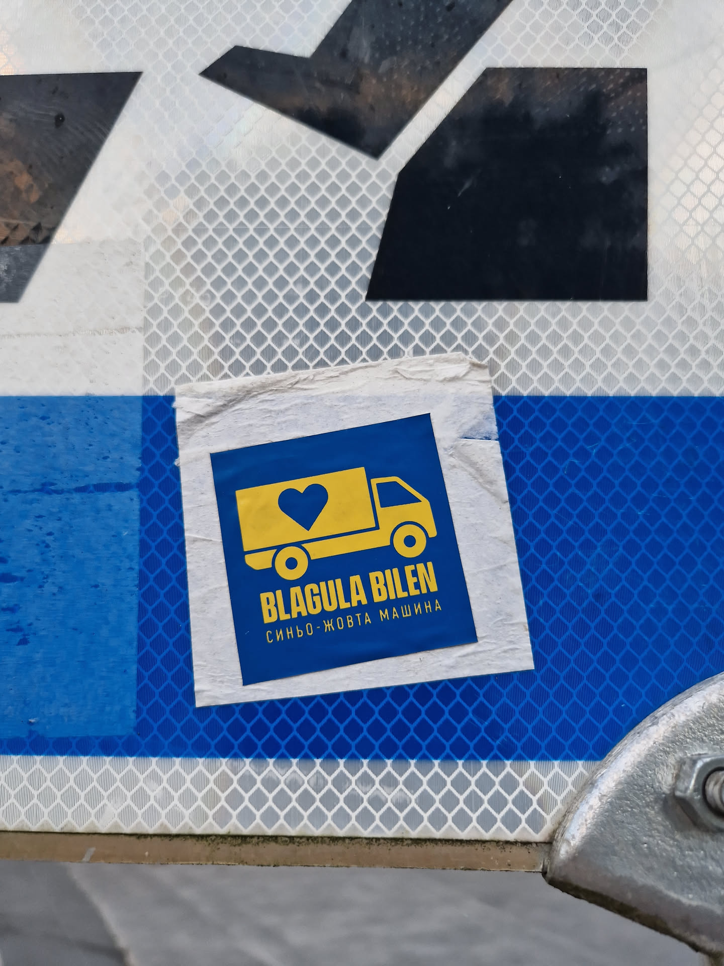 A blue and yellow sticker featuring a van with a heart on it. The text on the sticker says "Blagula Bilen" and "Синьо-жовта машина".