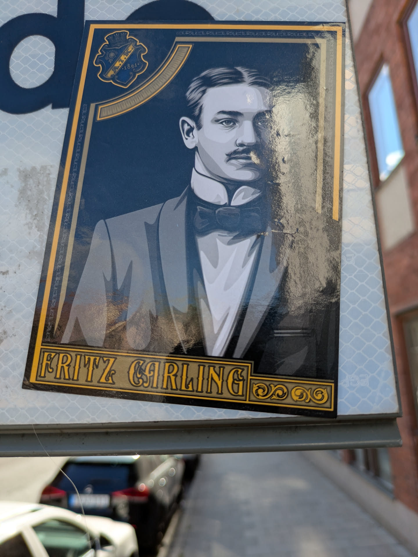 The sticker features a stylized, monochrome portrait of a man from a bygone era. He is depicted with slicked-back hair, a prominent mustache, and is dressed in formal attire, including a suit jacket, crisp white shirt, and a bow tie. The portrait is framed by an ornate gold border with decorative elements. Above the portrait, on the left side, is a blue and gold crest with the text 'AIK 1891+'. The overall aesthetic is reminiscent of vintage advertising or historical illustrations.