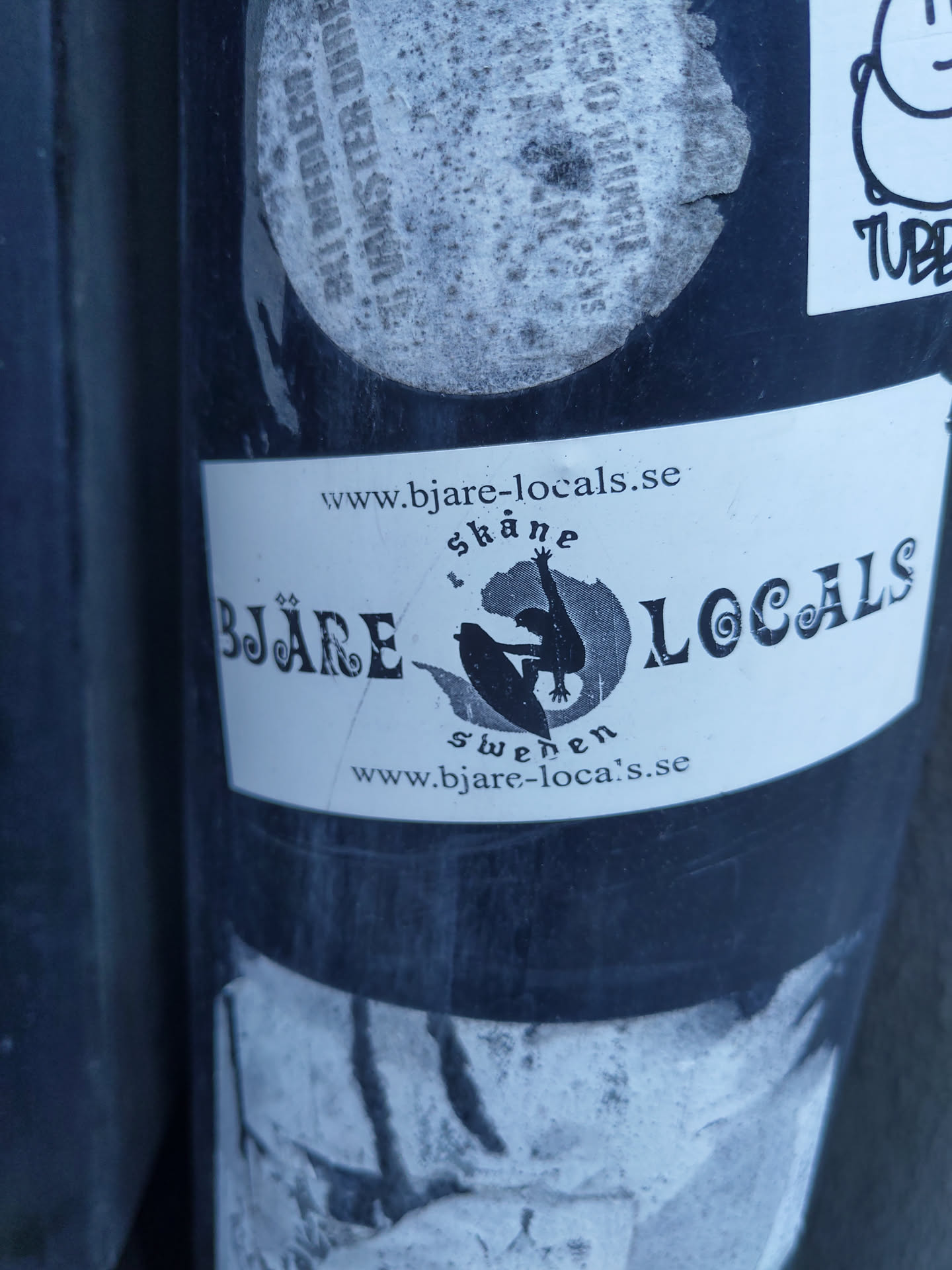 A black and white sticker featuring the Bjäre Locals logo, which includes a silhouette of a person surfing or doing a similar activity, with the text 'Bjäre Locals' and website address www.bjare-locals.se.  The sticker is adhered to a dark surface and appears slightly worn.