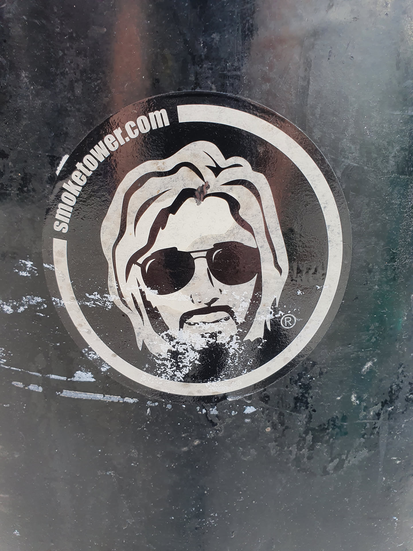 Black and white sticker featuring a stylized illustration of a person with long hair and sunglasses. The text "SmokeTower.com" is visible on the sticker.