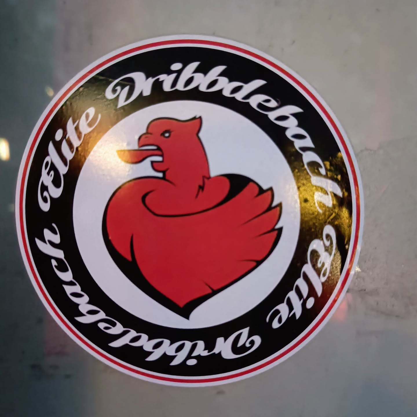 Round sticker featuring a red stylized bird illustration resembling a rooster or phoenix within a black circular border with the text Dribbdebach Elite written around it.