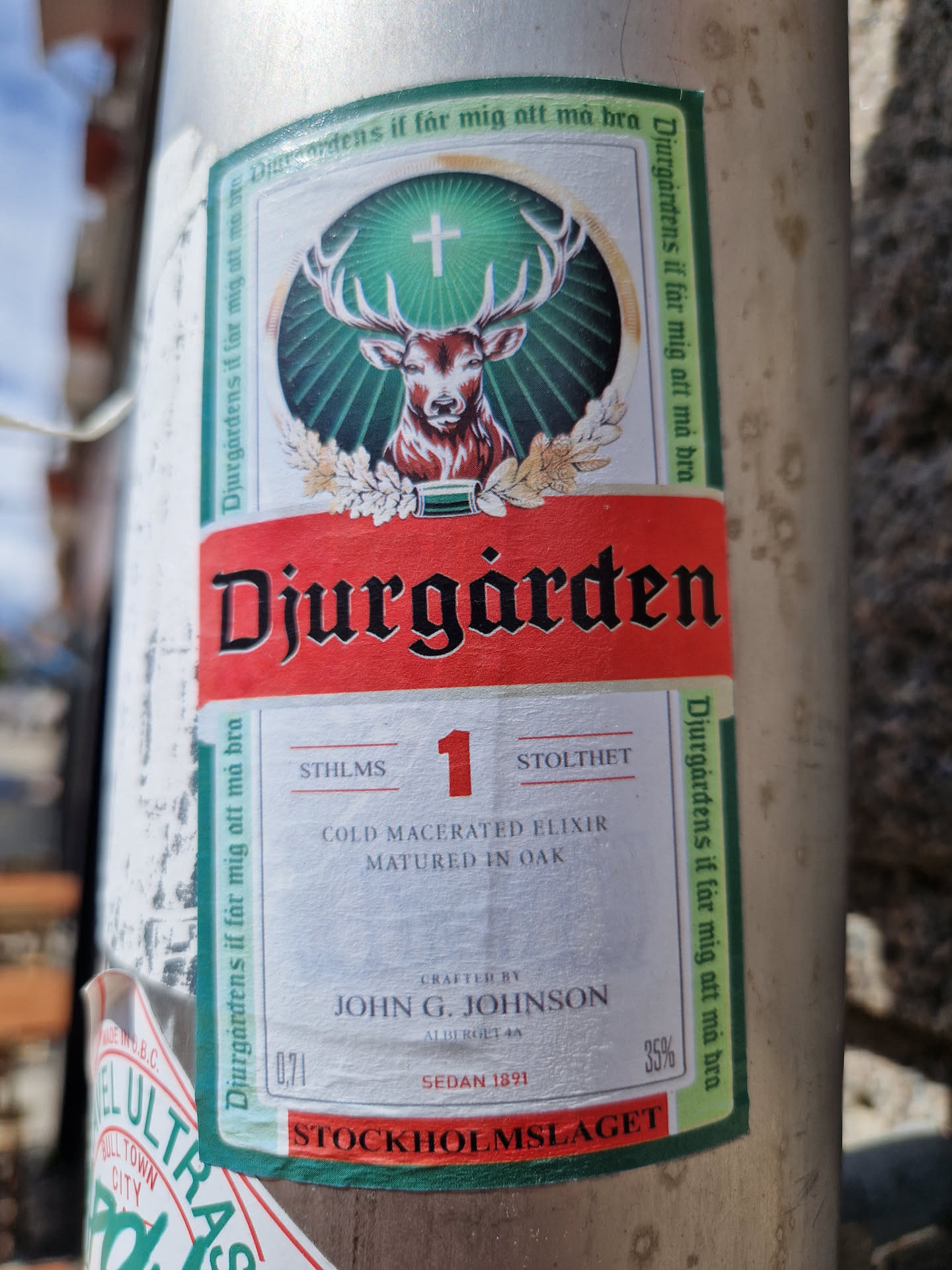 A sticker design featuring a stag and the text "Djurgården" along with other details like "Cold Macerated Elixir", "Matured in Oak", and "Stockholm Mislaget". It has a vintage look and might be associated with a drink or liquor brand.