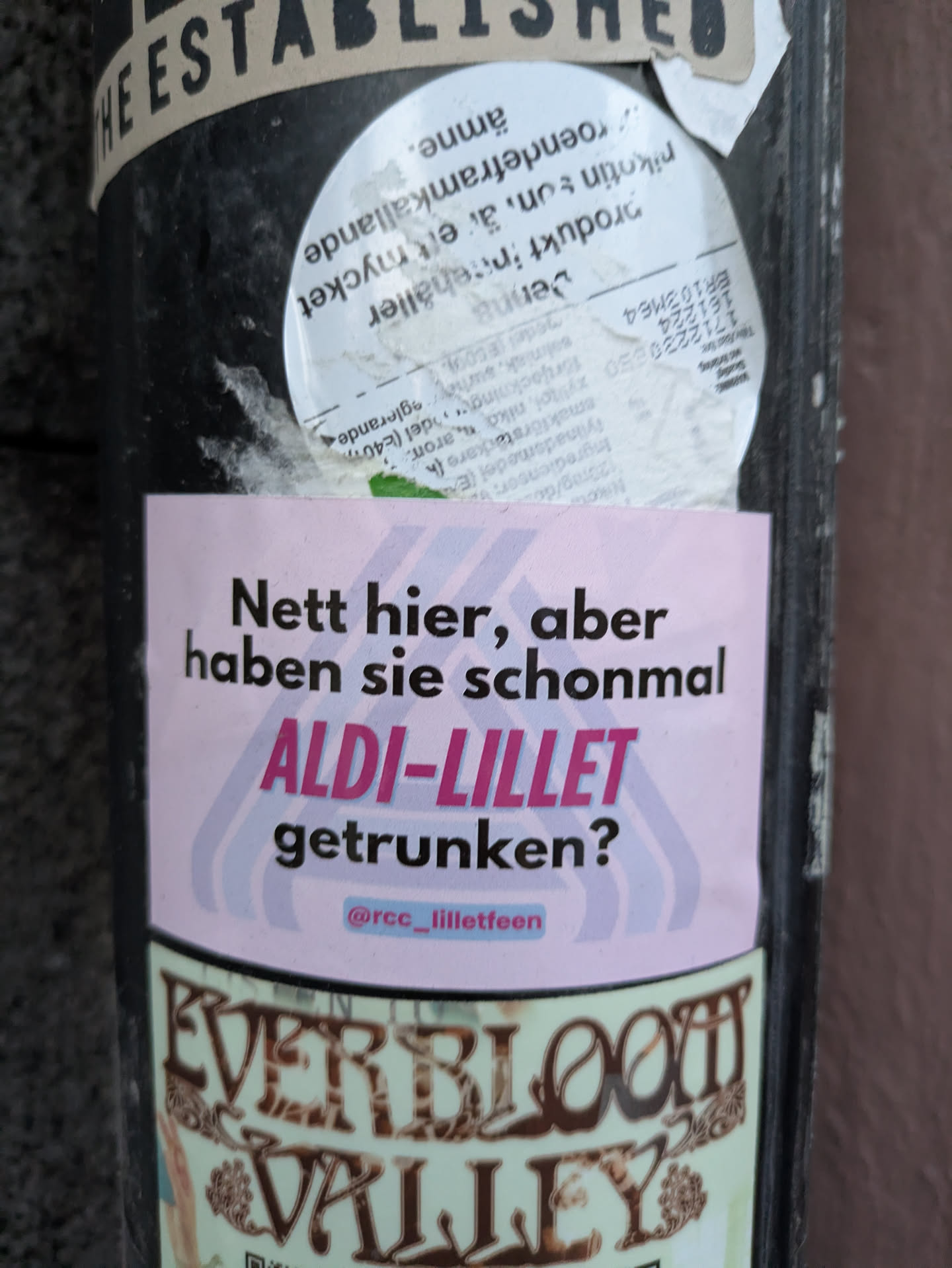 The sticker is predominantly pink with a pastel gradient. In the center, in bold black text, it asks 'Nett hier, aber haben sie schonmal ALDI-LILLET getrunken?'. Below this, in a smaller pink bubble, is the social media handle '@rcc_lilletfeen'. The phrase 'ALDI-LILLET' is highlighted in a bold, magenta-like color.