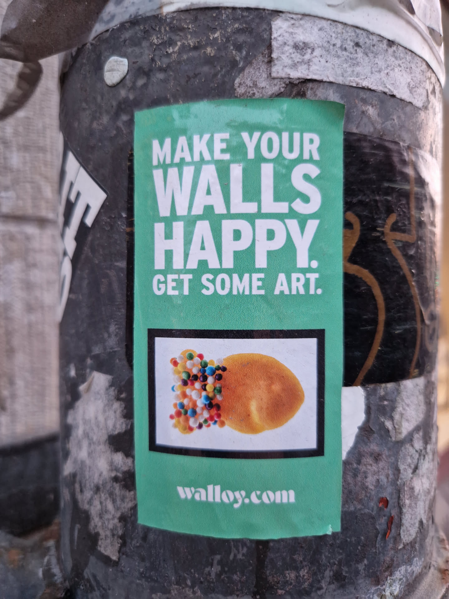 A teal and white sticker with the text 'Make Your Walls Happy. Get Some Art.' and a picture of a pastry with sprinkles. The website walloy.com is also visible at the bottom.