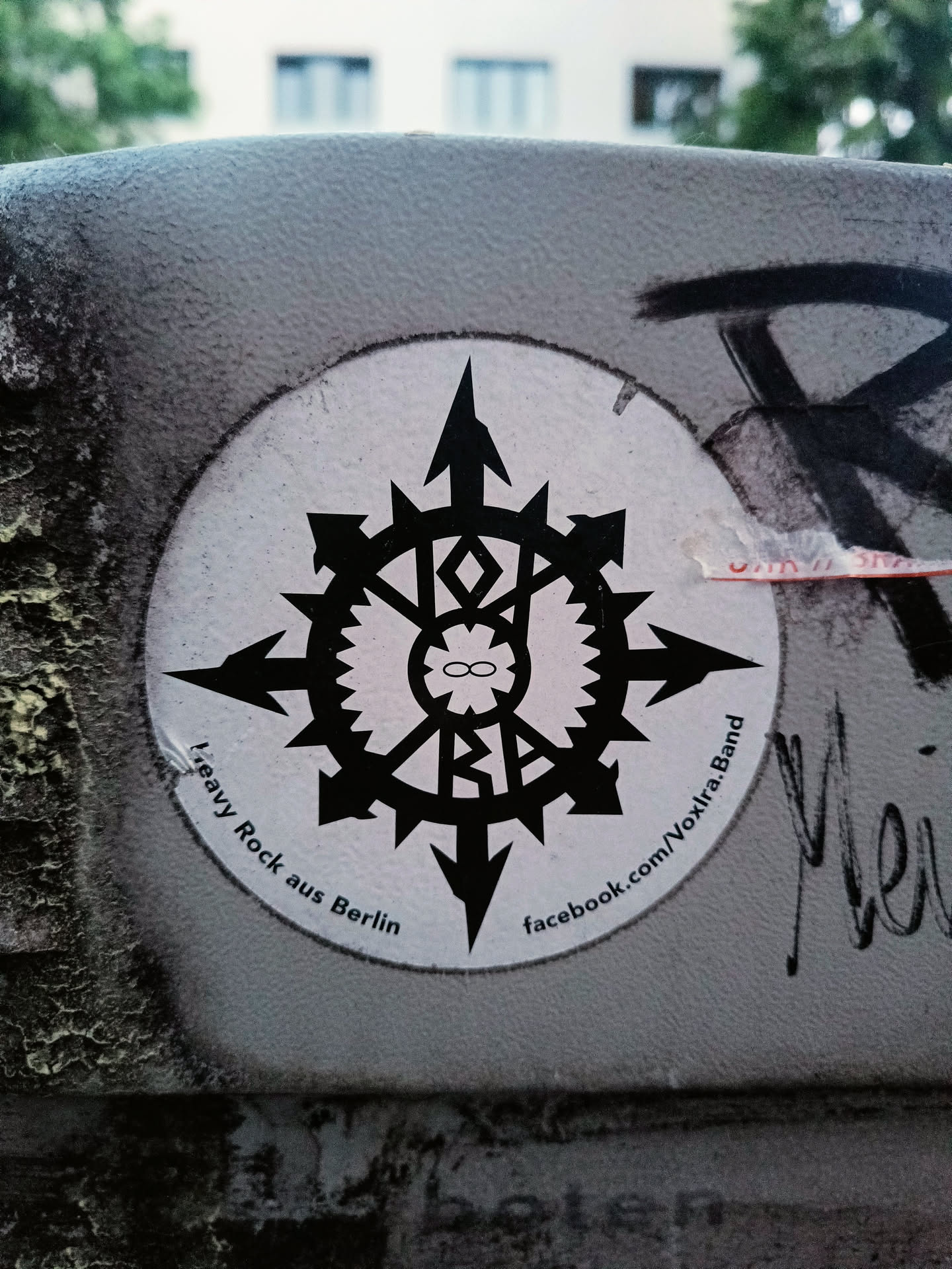 Round sticker with a black and white symbol resembling a compass or a stylized star.  The text around the symbol says "Heavy Rock aus Berlin" and includes a Facebook link. The central symbol contains what looks like the letters "VXR" within a circular design.