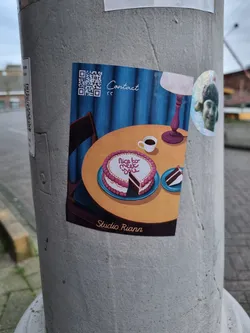 A sticker featuring an illustration of a heart-shaped cake on a table with a cup of coffee, a lamp, and a chair. The text "Nice to meet you" is written on the cake. The sticker has a QR code for contact and is signed "Studio Riann".