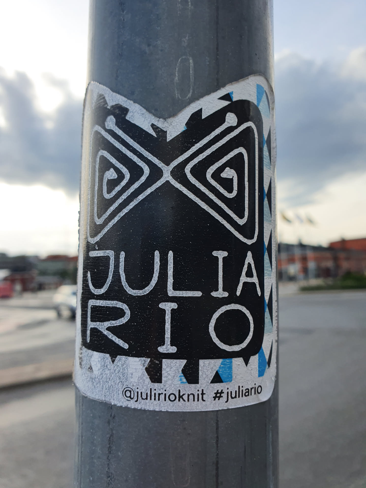 Black and white sticker with a geometric design and the name JULIA RIO written in a stylized font. The sticker also includes a social media handle and hashtag.