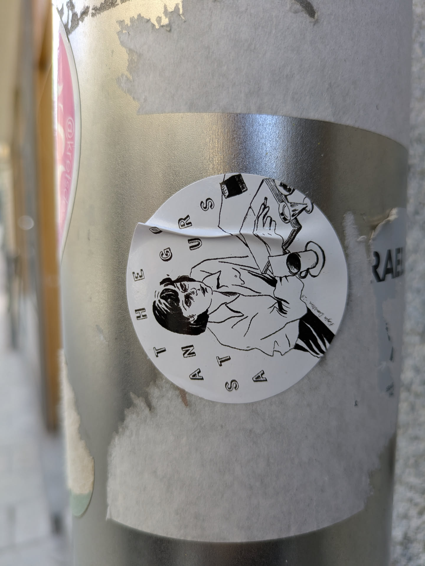 This round sticker features a black and white illustration of a person holding a cup, with a book and other items nearby. The sticker seems to be placed on a metallic pole or surface. The text "A STAN THE FUTURE" is printed around the illustration.