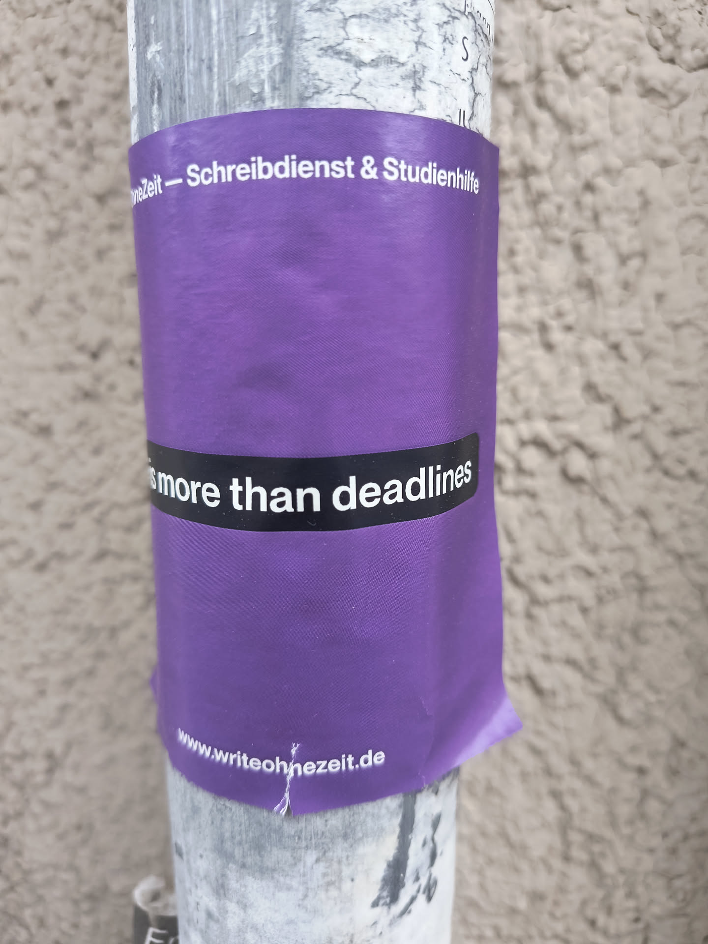 This sticker is primarily purple with a black banner displaying the message "Life is more than deadlines" in white text. The website address is printed at the bottom. The sticker is placed on a pole.