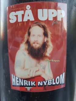 A sticker featuring a portrait of Henrik Nyblom with the text "Stå Upp för" above his name.  The background is red. There is also smaller text that seems to say "...hardcore för nägon/något" and a website address at the bottom.