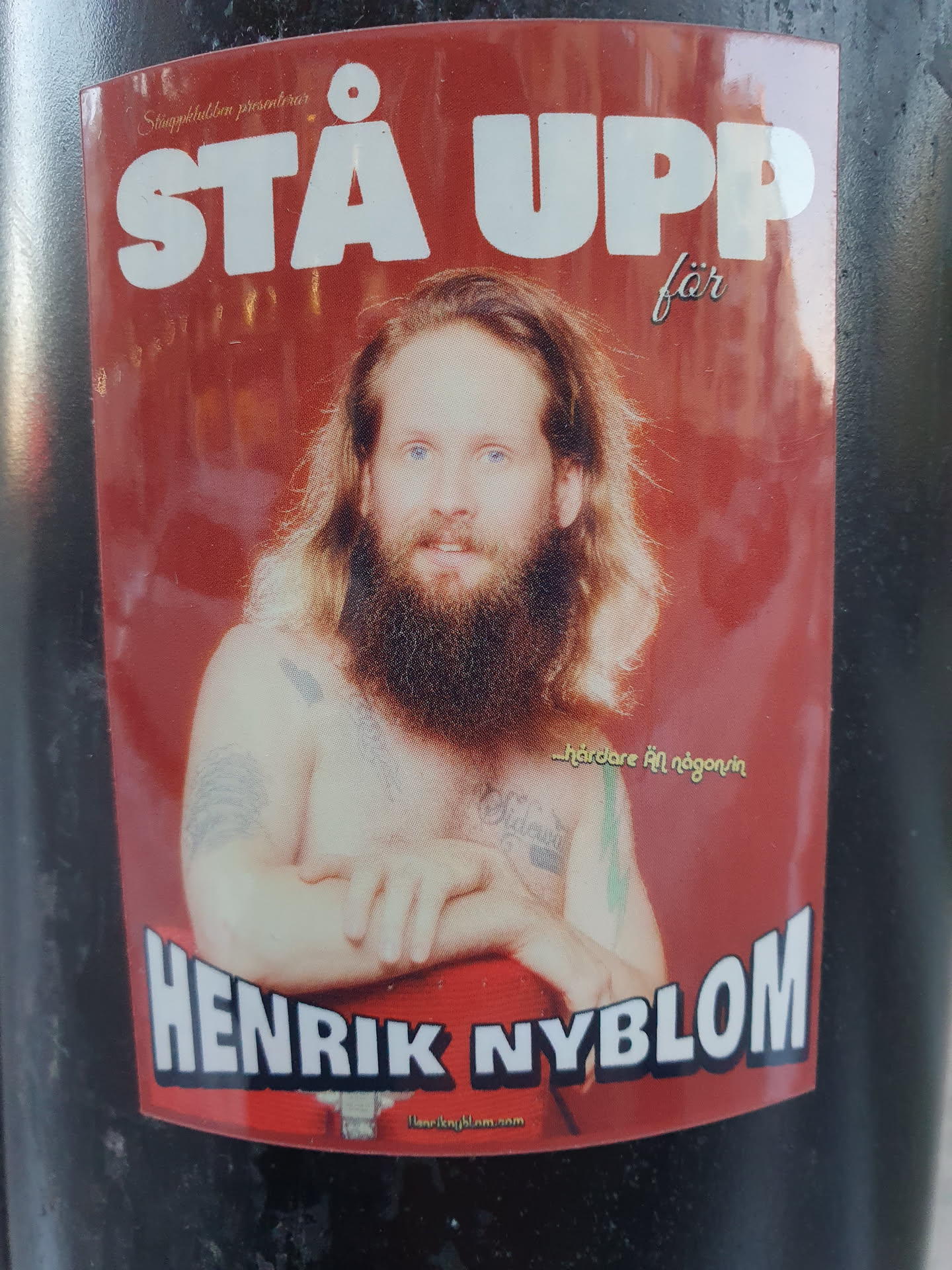 A sticker featuring a portrait of Henrik Nyblom with the text "Stå Upp för" above his name.  The background is red. There is also smaller text that seems to say "...hardcore för nägon/något" and a website address at the bottom.