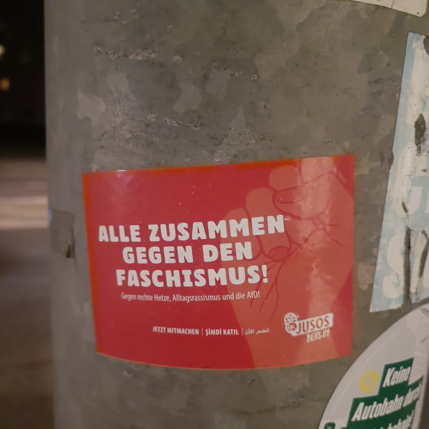A red sticker with a fist and the text "Alle zusammen gegen den Faschismus!" (Everyone together against fascism!). It also says to fight against right-wing hate, everyday racism, and the AfD (Alternative for Germany).  There is a logo for the Jusos Berlin (Young Socialists in Berlin) and the text includes calls to action in German, Turkish, and Arabic.