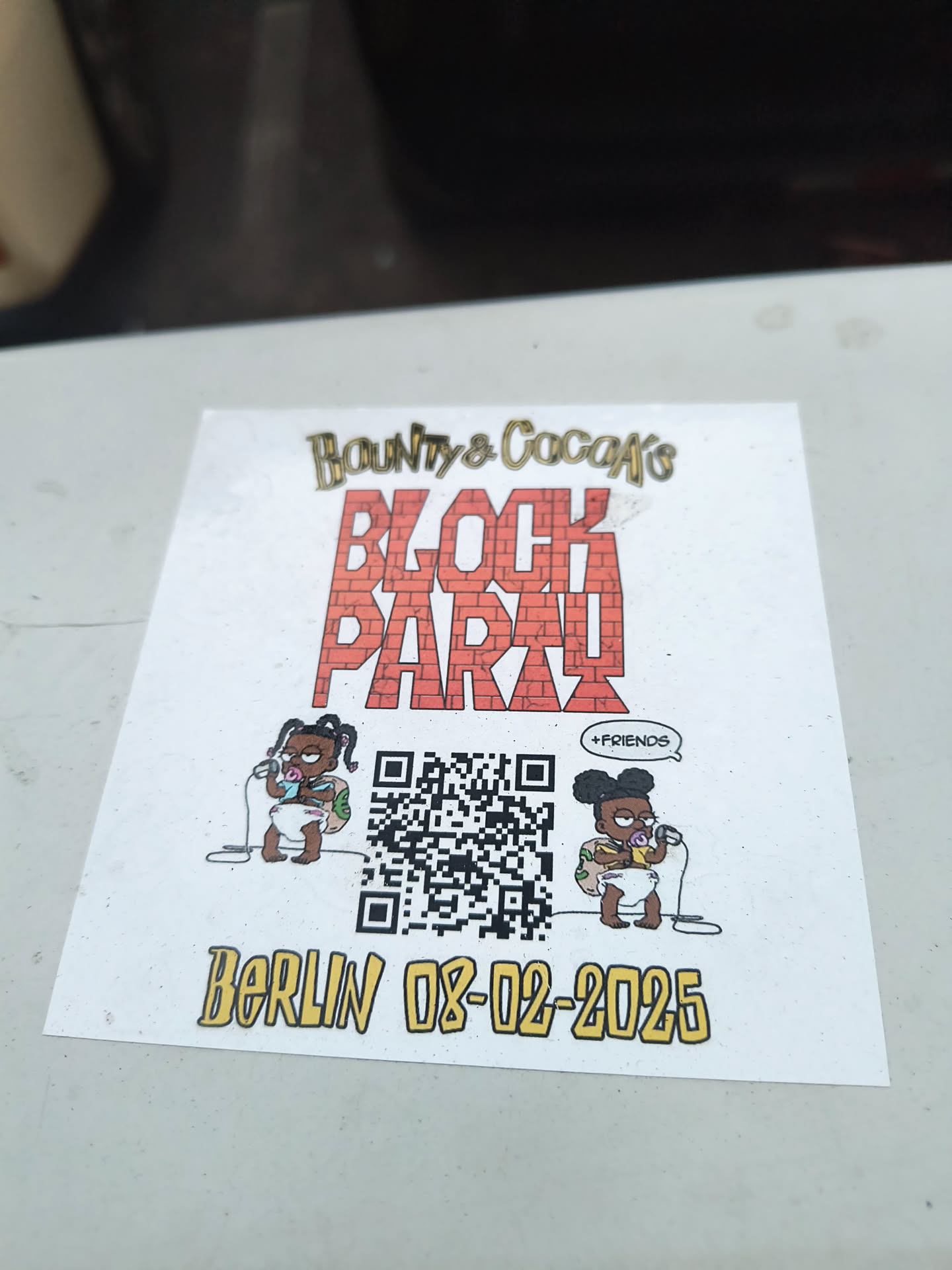 The sticker features cartoon babies resembling characters from 'The Simpsons' alongside a QR code and the event details.