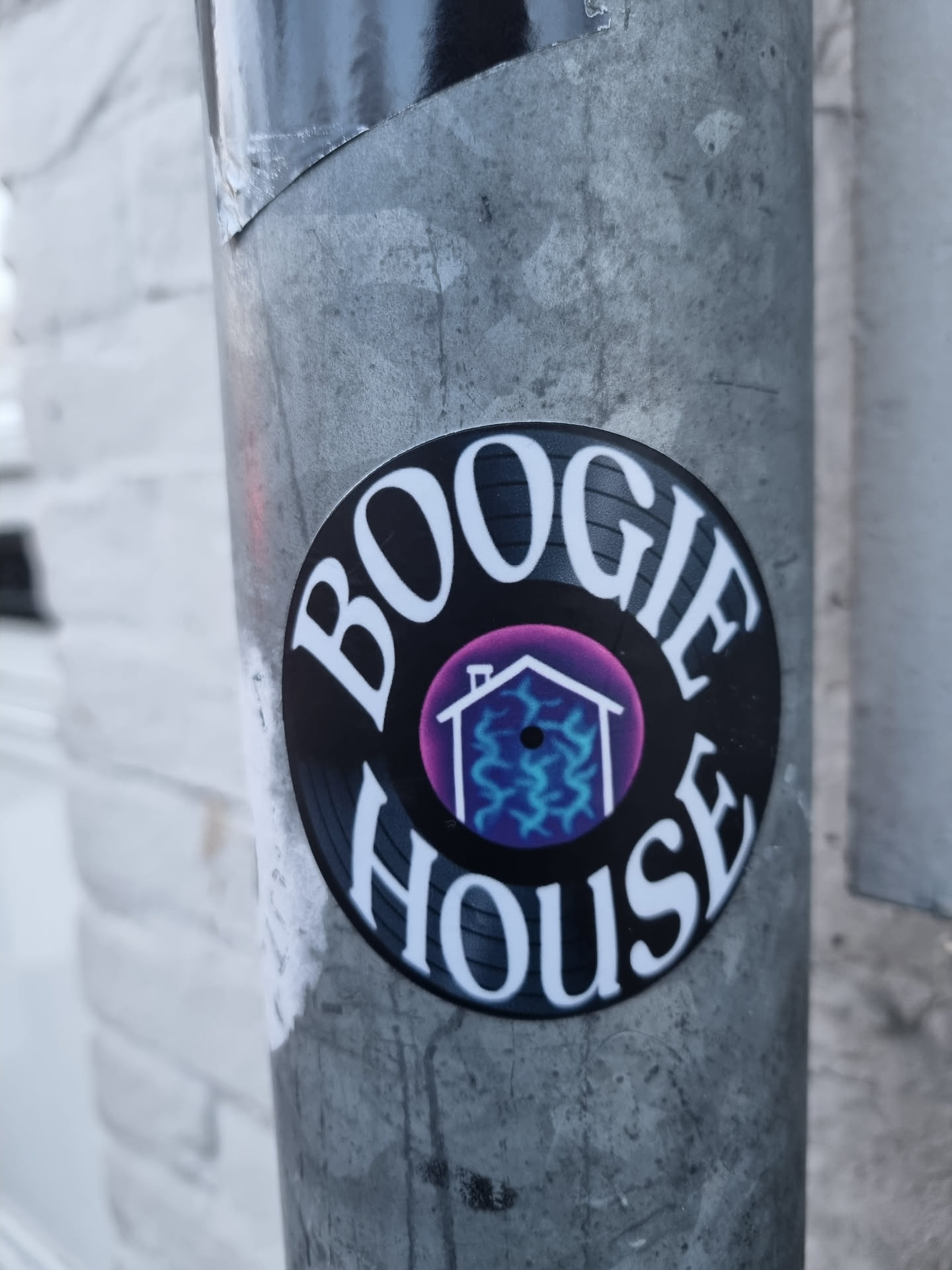 Round sticker imitating a vinyl record with the text "BOOGIE HOUSE" around a purple circle with a house icon inside. The house icon has blue lightning-like patterns inside.