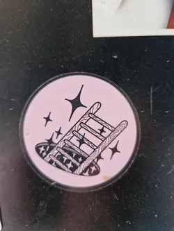 Pink circle sticker with a black line drawing of a ladder falling into a hole. There are small stars surrounding the ladder. 