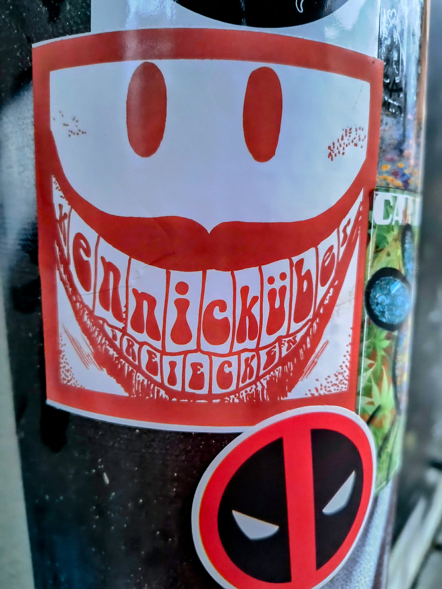 Red and white sticker with a smiling face. The text inside the mouth is difficult to read completely, but it seems to contain the word "ennickubes".