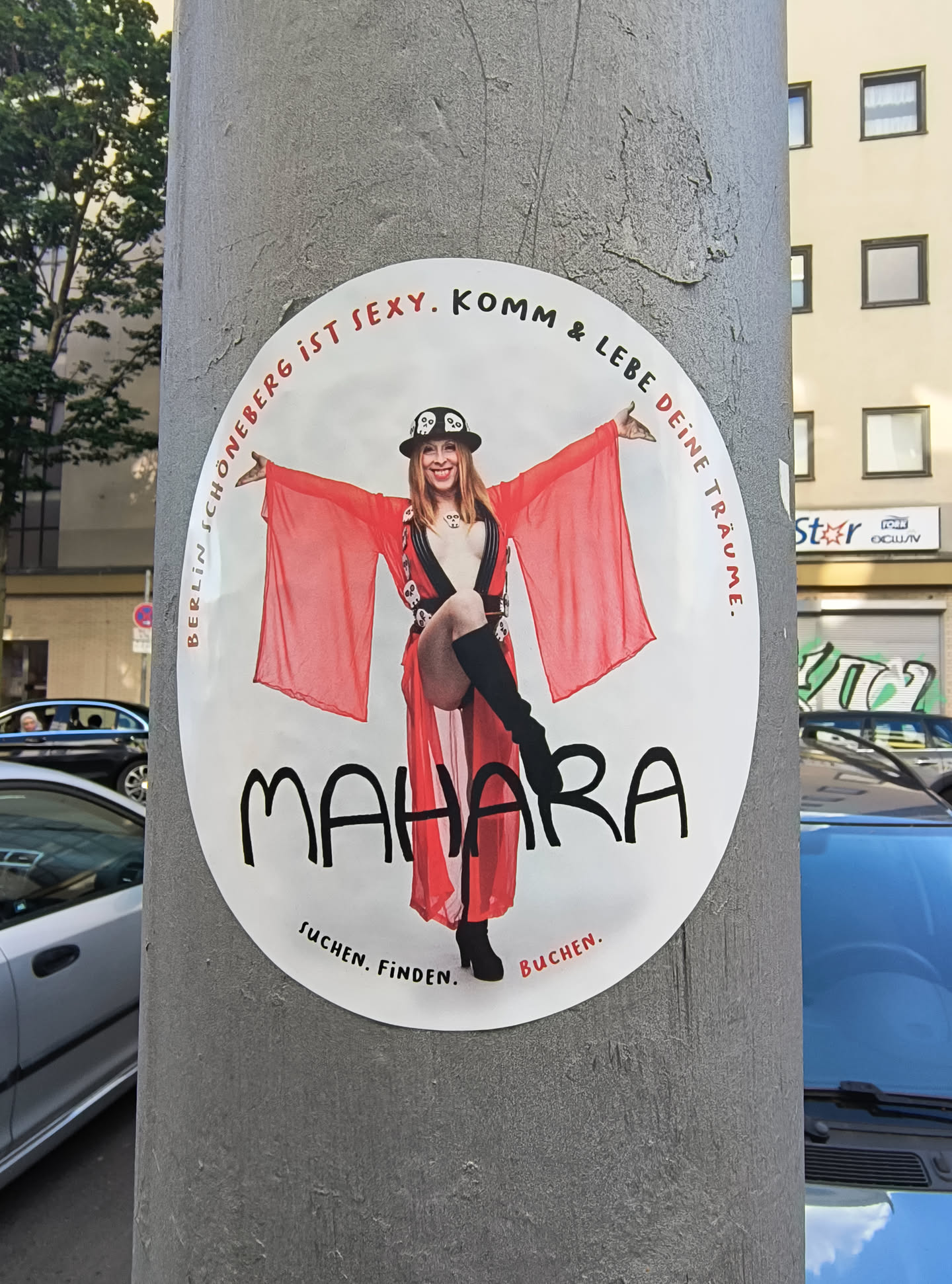 The sticker features an image of a woman in a red robe and a hat, with the words 'BERLIN SCHÖNEBERG IST SEXY. KOMM & LEBE DEINE TRÄUME.' and 'MAHARA' printed on it. The text 'SUCHEN. FINDEN. BUCHEN.' is at the bottom of the sticker.