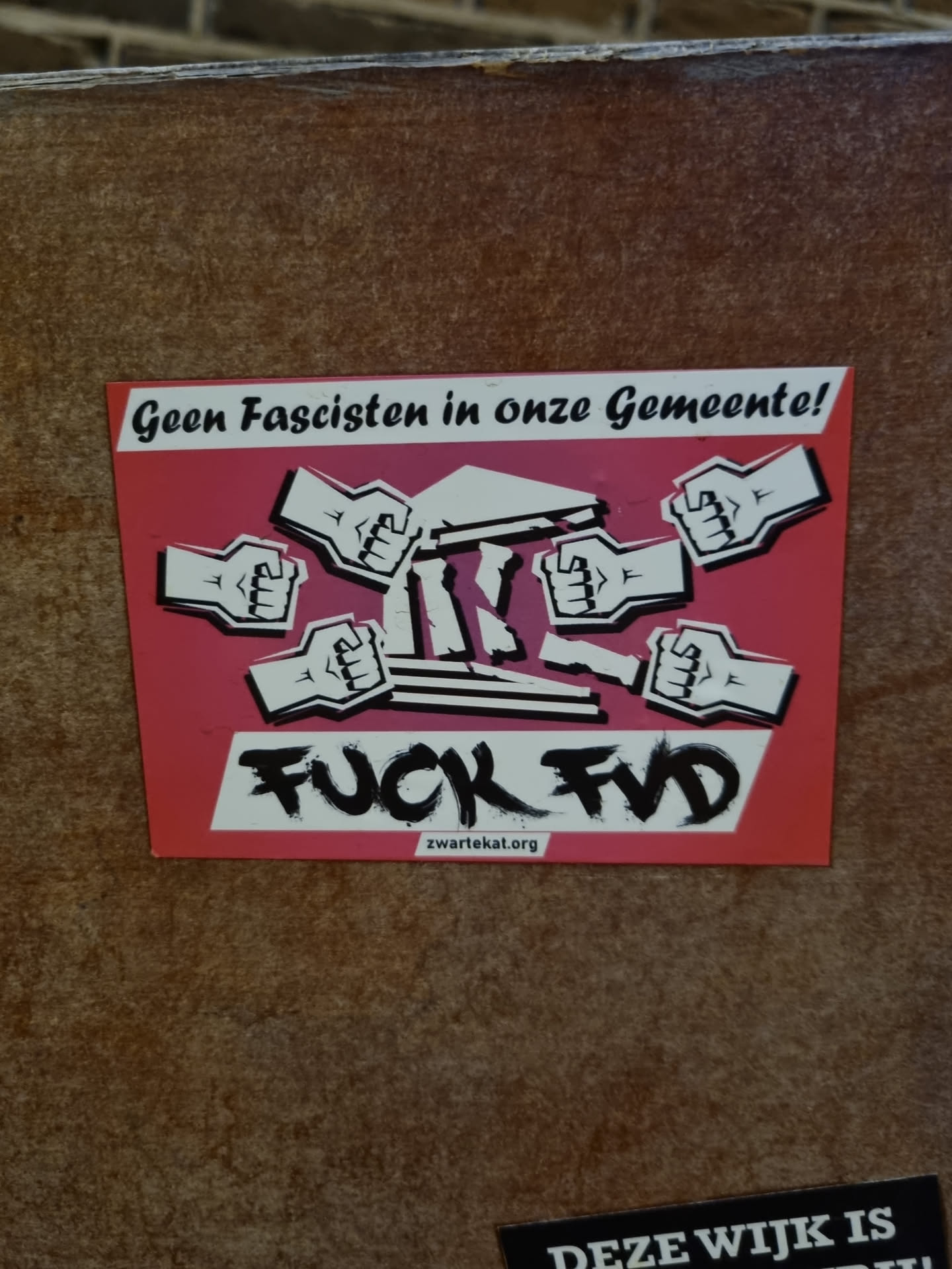 A sticker with a strong anti-fascist message. It features several fists smashing a representation of a classical building, symbolizing the rejection of fascism. The text includes the phrase "Geen Fascisten in onze Gemeente!" (No Fascists in our Municipality!) and "FUCK FVD" (FVD likely refers to a political party). A website address is also present: zwartekakat.org.