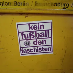 A sticker with the text "Kein Fußball den Faschisten" (No football for fascists) in German. It features a logo that seems to be related to a Berlin-based sports club.