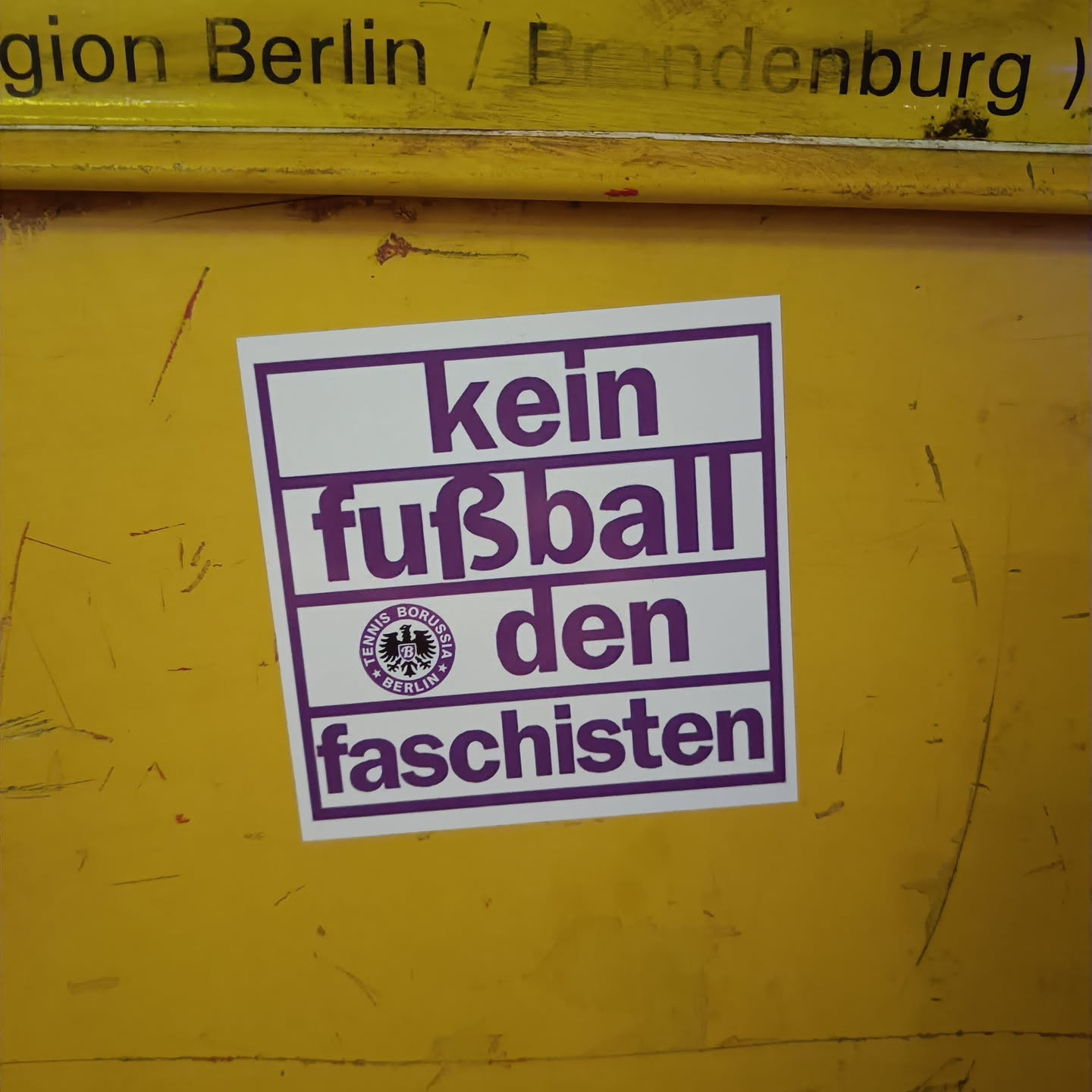 A sticker with the text "Kein Fußball den Faschisten" (No football for fascists) in German. It features a logo that seems to be related to a Berlin-based sports club.