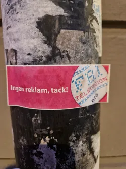 A sticker with a pink background and the text 'Ingen reklam, tack!' (Swedish for 'No ads, thanks!') and a logo of a TV with cross-stitch style.  The sticker appears to be anti-advertising.