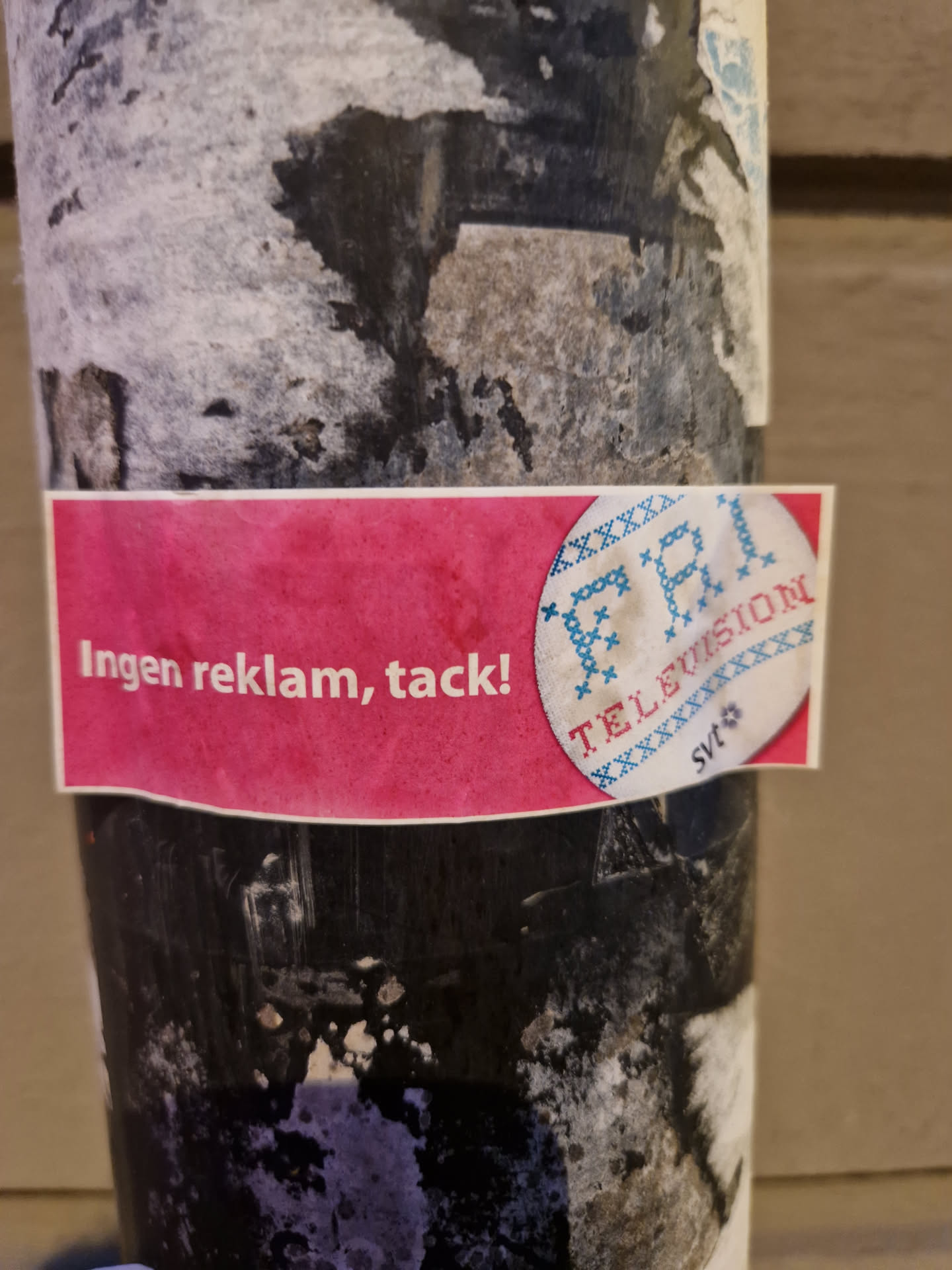 A sticker with a pink background and the text 'Ingen reklam, tack!' (Swedish for 'No ads, thanks!') and a logo of a TV with cross-stitch style.  The sticker appears to be anti-advertising.