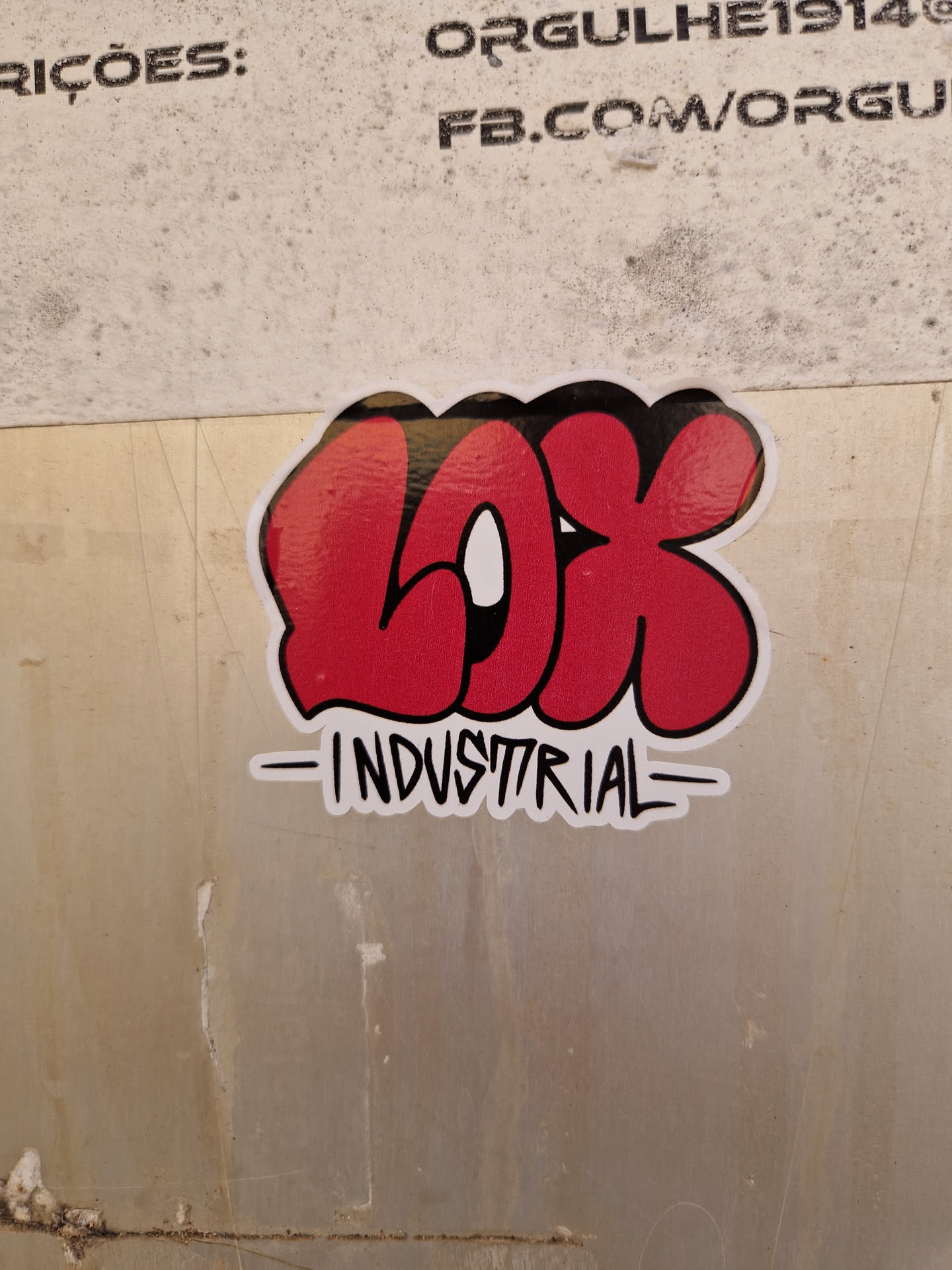 Red graffiti sticker with the letters LOK in bubble letters and the word INDUSTRIAL underneath. The sticker is placed on a beige wall.