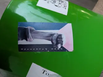 A sticker featuring a fist and the text 'Free Palestine'. The fist is depicted in gray tones over a background with blue, white, and pink hues. The text 'FREE PALESTINE' is printed below the image.