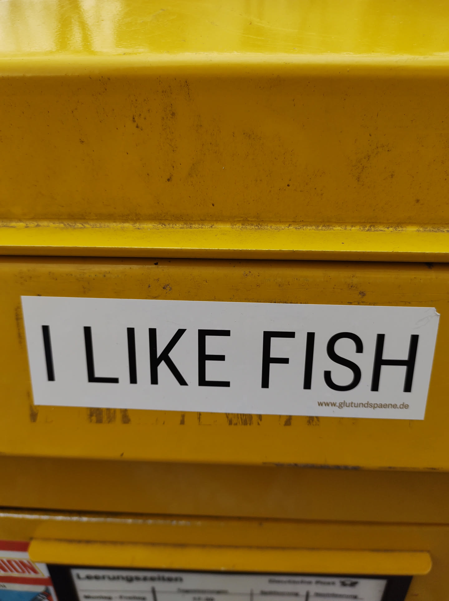 A white sticker on a yellow surface with the text "I LIKE FISH" and a website address at the bottom. 
