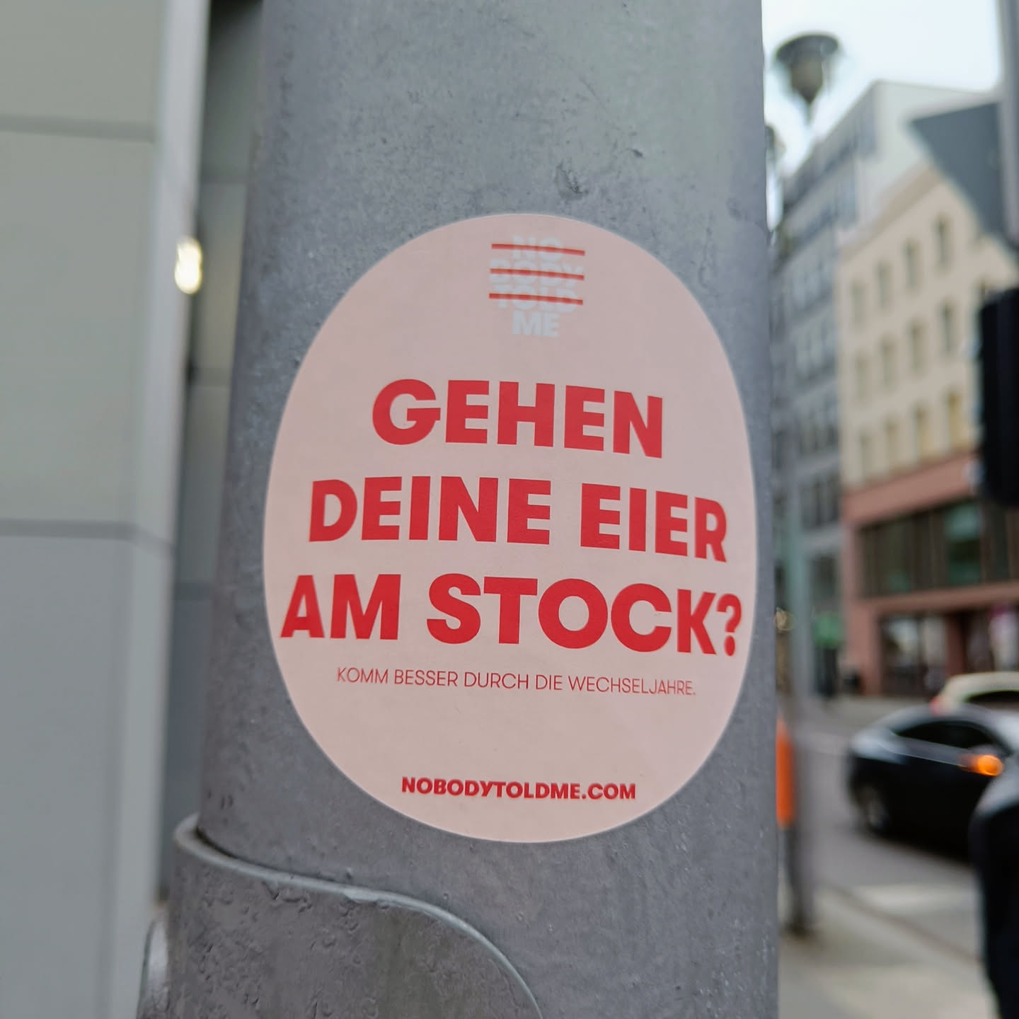 A round sticker with red text on a light pink background. The text says "Gehen deine Eier am Stock?" which translates to "Are your eggs going to stock?" in English. Below it is a smaller text that says "Komm besser durch die Wechseljahre" which translates to "Get through menopause better". At the bottom, there is a website address: nobodytoldme.com